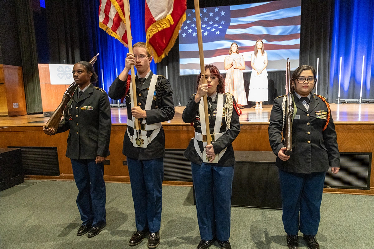 four students in military uniforms presenting a flag